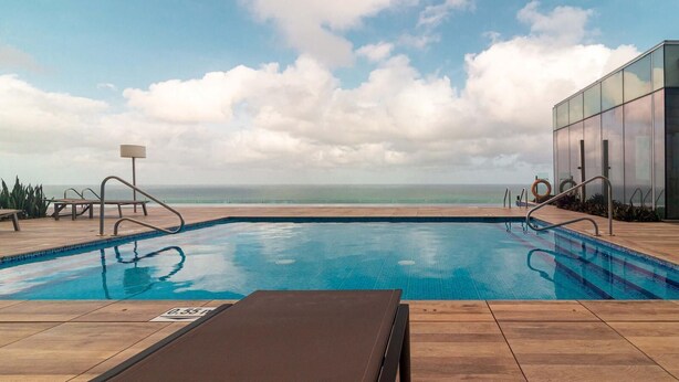 A swimming pool with a view of the ocean, a wooden deck, and a glass building. - Premium suite 25th floor (Cartagena de Indias)