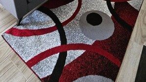 Un salon moderne avec un canapé d’angle gris, des coussins décoratifs rouges et blancs et un tapis à motifs.