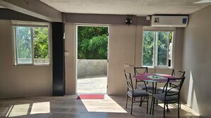 Une pièce avec une table et des chaises en verre, un tapis rouge à l’entrée et deux fenêtres donnant sur un paysage verdoyant.