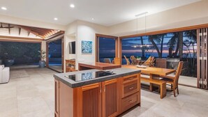 Une cuisine moderne dotée d’un grand îlot central, de meubles en bois et offrant une vue sur la plage au coucher du soleil.
