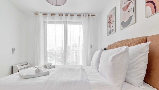 A hotel room with a bed, white curtains, a view through the window, and artwork on the wall. - Pleasant apt with balcony -6P-Proche Disney/Paris (Champigny-sur-Marne)