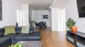 Una sala de estar moderna con un sofá de cuero negro, una mesa de comedor con sillas y una cocina al fondo.