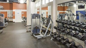 Un gimnasio con equipo de ejercicio, estantes para pesas y espejos.