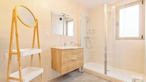 A bathroom with a wooden vanity, a mirror, a shower, and a window.