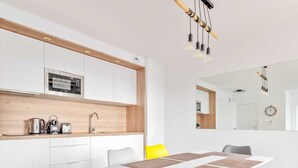 A modern kitchen with a microwave, kettle, and toaster on the counter. There is a dining table with chairs and a mirror above it.