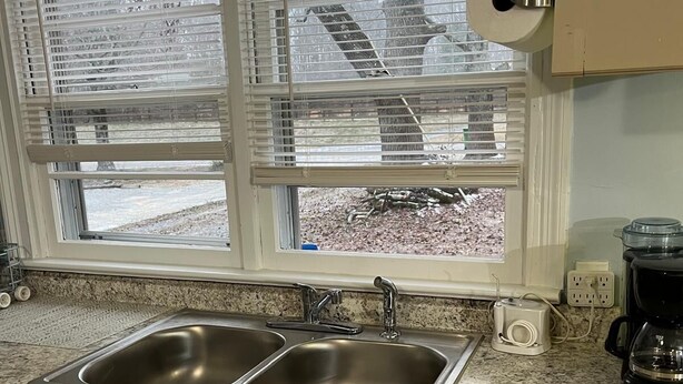 A kitchen with two stainless steel sinks, a window with blinds, and a coffee maker on the counter. - The Holy Family of Nazareth (Cullman)