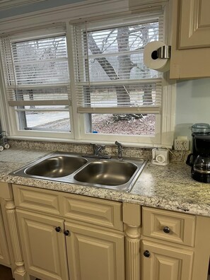 A kitchen with two stainless steel sinks, a window with blinds, and a coffee maker on the counter.