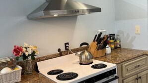 A kitchen with a white stove, stainless steel range hood, granite countertop, and light blue walls. - The Holy Family of Nazareth (Cullman)