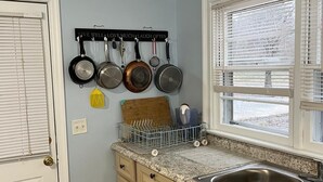 A kitchen with light blue walls, a window with blinds, a sink, and a dish rack. - The Holy Family of Nazareth (Cullman)