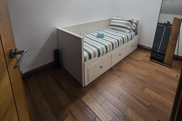 A small, single-bed room with a wooden floor, a white headboard, and striped bedding.