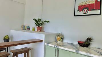 Une cuisine avec un bar en bois, des meubles de couleur verte, une plante en pot, un vase et un tableau encadré représentant un camion rouge.