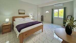 A bedroom with a bed, bedside tables, a nightstand, a window with curtains, a wall-mounted air conditioner, and a potted plant. - Hillside Escape- Private Pool & Breathtaking Sunset Over the Town (Bequia)