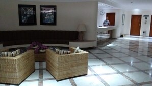 A lobby with a curved seating area, a reception desk, and a clock on the wall. - Apê da Mi (Guaruja)