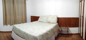 A single bed with a floral bedspread, a wooden headboard, and a small wooden stool. - Apê da Mi (Guaruja)
