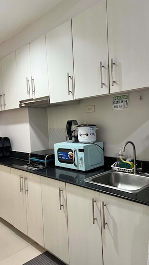 A kitchen with white cabinets, a microwave, a slow cooker, and a sink.