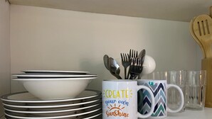A kitchen shelf with stacked white plates, a white mug with a motivational quote, and a patterned mug. - MOA-View 1BR - 5 min Walk to MOA Arena (Pasay)