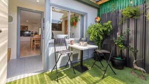 Eine Terrasse mit Tisch und Stühlen, ein kleiner Gartenbereich mit Pflanzen und Blick ins Haus.