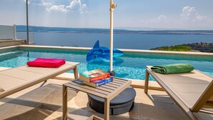 An infinity pool with a view of the sea, lounge chairs, a yellow umbrella, and a blue inflatable shark. - Vacation home Marika by Interhome (Crikvenica/Dramalj)
