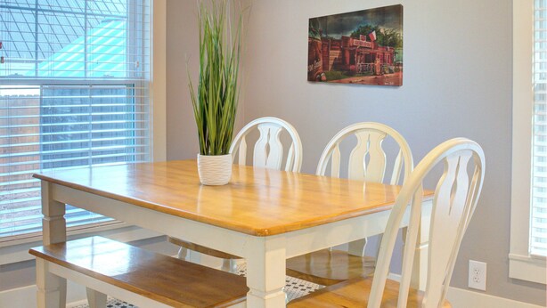 Un comedor con mesa de madera, sillas blancas, una planta en maceta y un ventilador de techo.