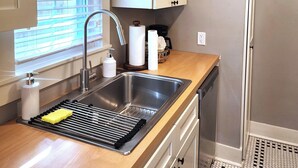 Una cocina con un lavamanos de acero inoxidable, encimera de madera y armarios blancos.