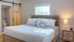 Un dormitorio con cama, mesita de noche, ventana y puerta.