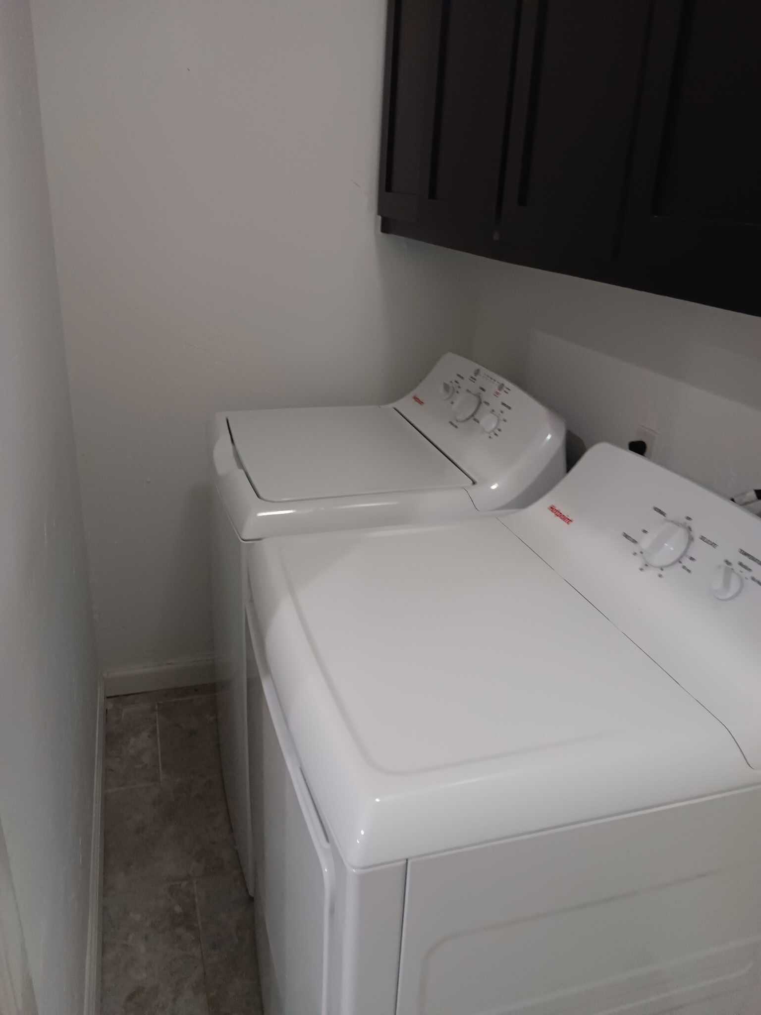 A laundry area with two white washing machines and a dark cabinet above them.