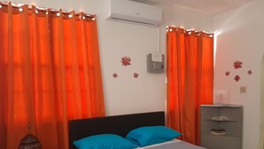 Ein Schlafzimmer mit einem Bett, orangefarbenen Vorhängen, einem kleinen Tisch mit einer Vase und einer grauen Kommode.