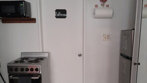 Eine kompakte Küche mit Herd, Backofen, Mikrowelle und Kühlschrank. Auf der Tür ist ein Schild mit der Aufschrift 'Badezimmer' zu sehen.