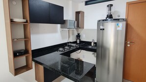 A compact kitchen with a black countertop, a built-in microwave, a coffee maker, and a stainless steel refrigerator. - Flat Bela Vista Porto de Galinhas 206bLP (Ipojuca)