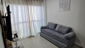 A living room with a grey sofa, a white ceiling light, and a framed quote on the wall. - Flat Bela Vista Porto de Galinhas 206bLP (Ipojuca)