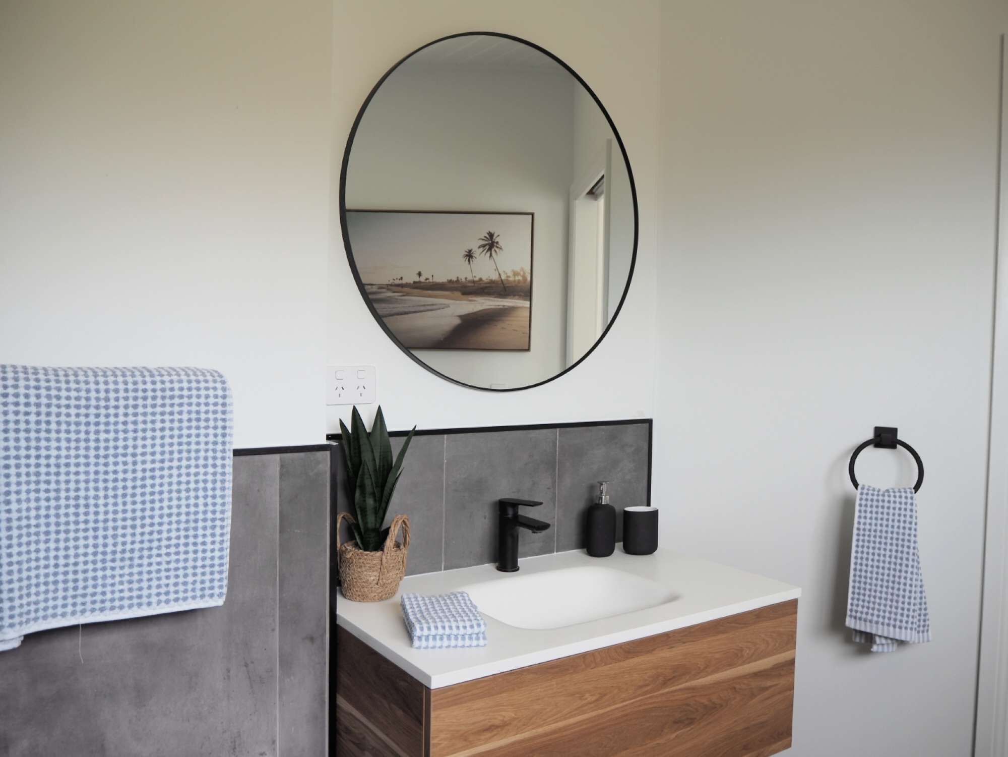 Un baño moderno con tocador de madera, un espejo redondo y un perchero para toallas.