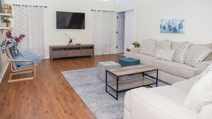 Amplia sala de estar con televisor grande, sofá, mesa de centro y piso de madera.