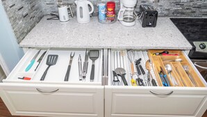 Una cocina con encimera de granito, armarios blancos y un organizador de cajones con utensilios.