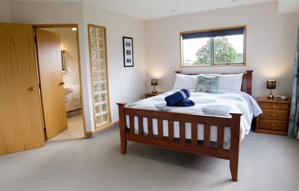 A bedroom with a wooden bed, a nightstand with a lamp, a window with a view, and a door leading to another room.