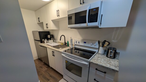 A compact kitchen with white cabinets, a built-in microwave, a stove, and a sink. - Cozy & Private Suite w/ Private Entrance & Parking (Richmond Hill)