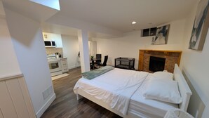 A bedroom with a bed, a fireplace, a desk, and a kitchen in the background. - Cozy & Private Suite w/ Private Entrance & Parking (Richmond Hill)
