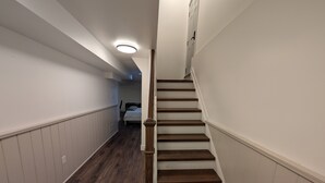 A narrow hallway with wooden flooring and white walls, leading to a staircase with wooden steps and a white banister. - Cozy & Private Suite w/ Private Entrance & Parking (Richmond Hill)