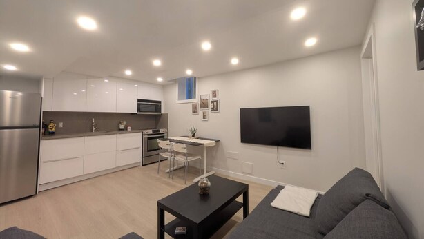 A modern apartment with a kitchen, dining area, and living room. It includes a flat-screen TV, a sofa, and a coffee table.