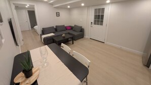 A modern living room with a grey sofa, a dining table with chairs, and a small potted plant.
