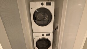 A compact, white laundry room with two stacked washing machines, one above the other, and a visible electrical outlet on the wall.