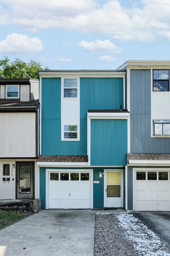 Une rangée de maisons de ville avec une porte de garage centrale, une petite fenêtre et une boîte aux lettres.