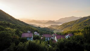 A valley with houses surrounded by dense forest and mountains in the background. - Lafite Apple B&B (Hangzhou)