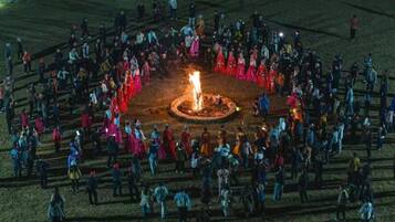 A large outdoor gathering around a central fire with people standing in a semi-circle.