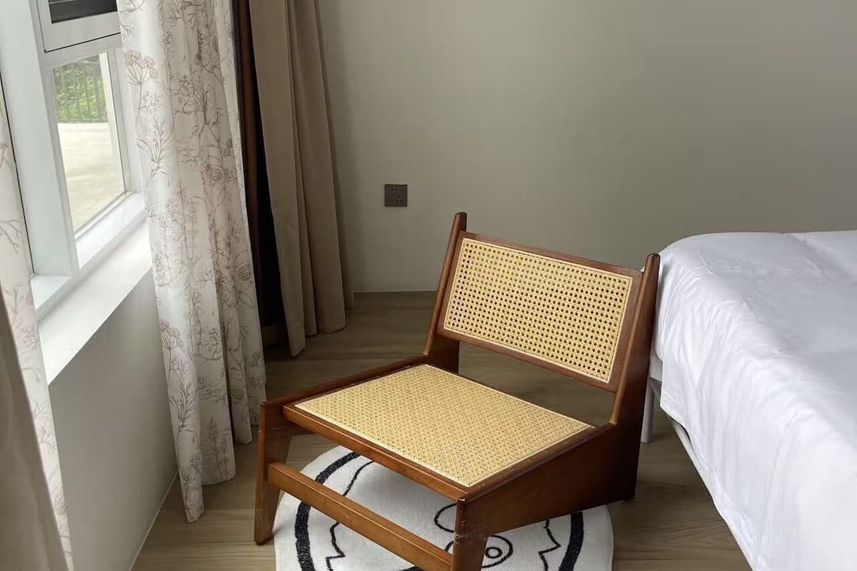 Quarto com cadeira de madeira e encosto trançado, cama com roupa de cama branca e tapete com padrão preto e branco.
