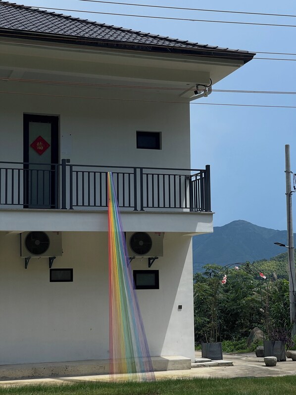 A two-story building with a balcony, air conditioning units, and a mountain in the background.
