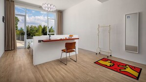 Una habitación moderna con suelo de madera, un escritorio blanco con una silla, un ventanal y vistas a zonas verdes.