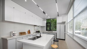 Una cocina moderna con armarios blancos, una isla central con taburetes, un horno empotrado y una ventana con vista a follaje.