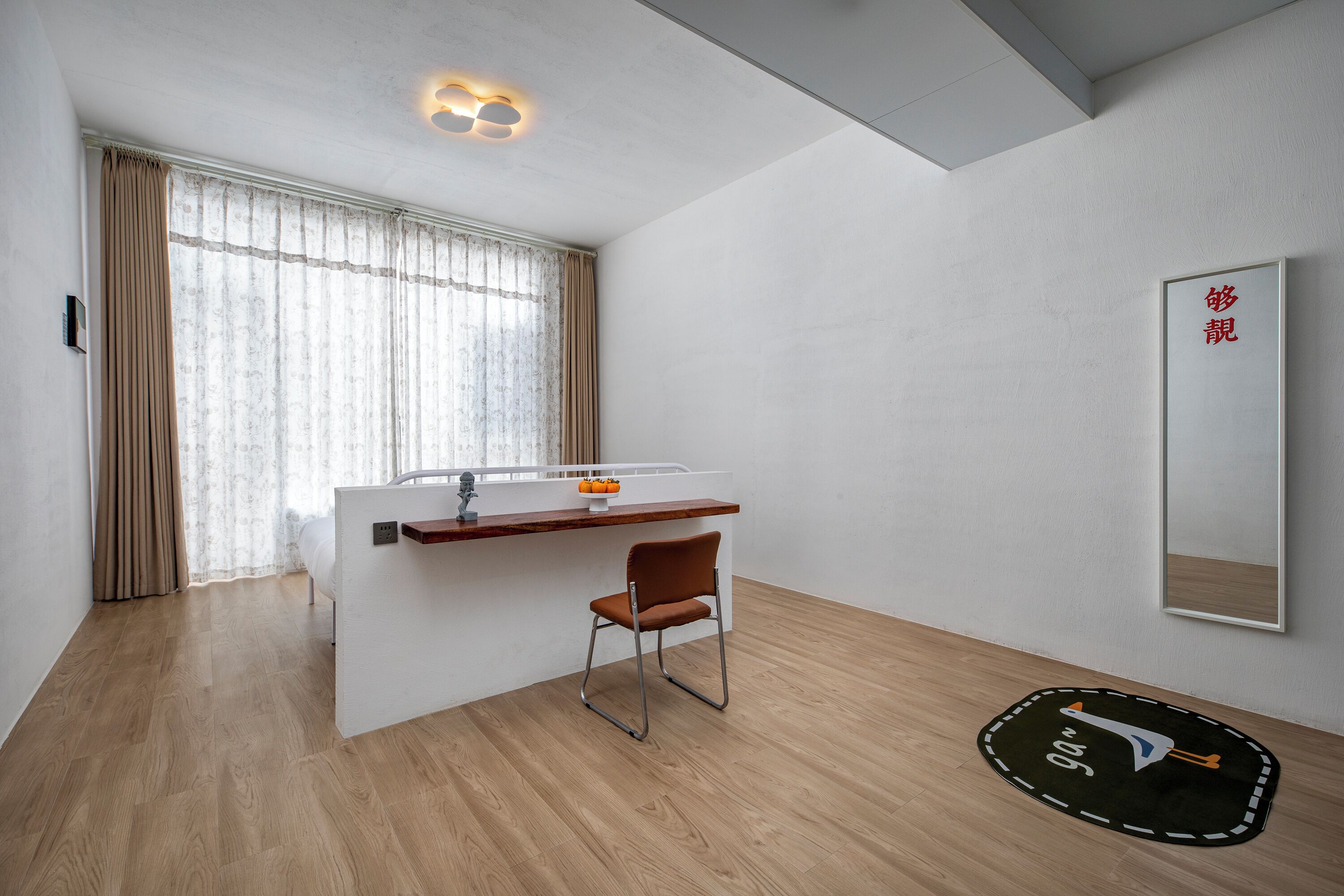 A modern hotel room with a wooden floor, a small desk with a chair, a large window with curtains, and a wall-mounted mirror.