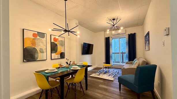 Una sala de estar moderna con comedor, que presenta piso de madera, un sofá, un sillón azul y arte abstracto en la pared.