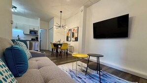 A living room with a sofa, a coffee table, a TV mounted on the wall, and a dining area with chairs and a table. - Cute little apartment in the city center (Québec)